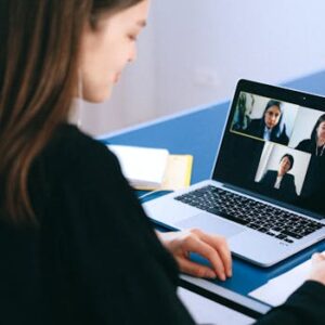 A woman engaging in a video conference using a laptop at home, taking notes.